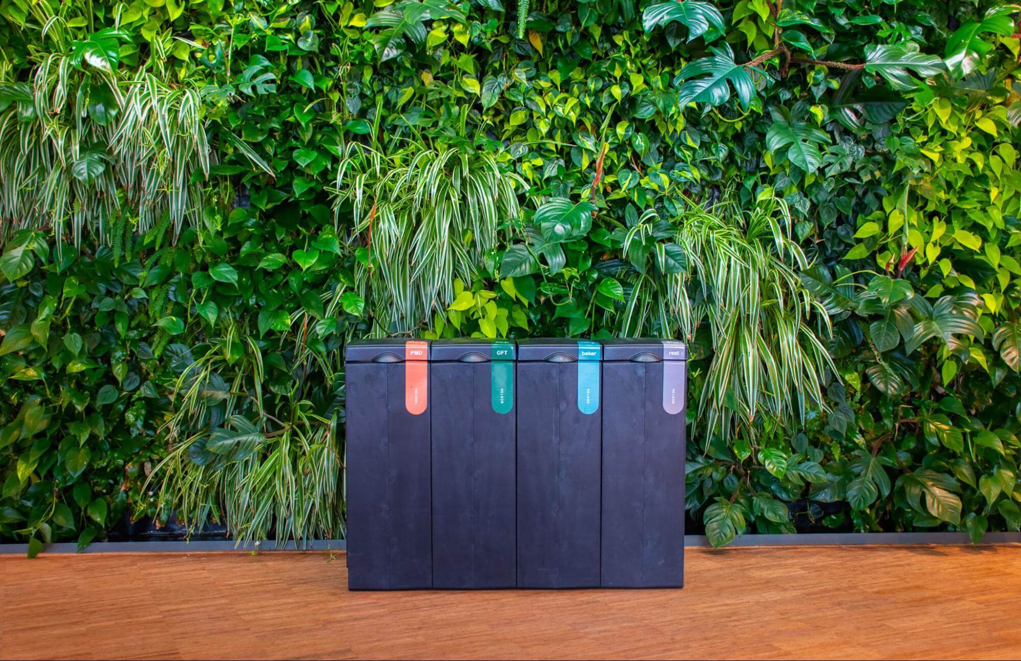 Zwarte afvalscheidingsprullenbak tegen een groene plantenwand